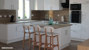 A modern kitchen with white cabinetry, a wooden island with bar stools, a microwave, and a built-in oven. - Villa ‘leticas’, its Private Pool in the Sun of Lot et Garonne (Prayssas)