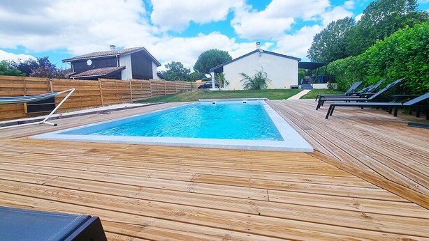 A wooden deck with a rectangular swimming pool, surrounded by a wooden fence and a white building. - Villa ‘leticas’, its Private Pool in the Sun of Lot et Garonne (Prayssas)