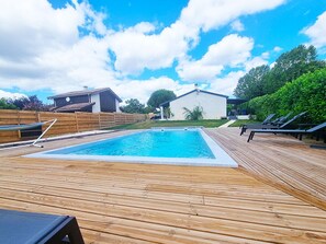Um deck de madeira com uma piscina retangular, cercado por uma cerca de madeira e um edifício branco.