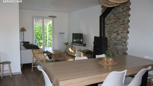 A modern kitchen with a wooden table, white chairs, a TV, and a stone wall. - Villa ‘leticas’, its Private Pool in the Sun of Lot et Garonne (Prayssas)