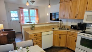 A compact kitchen with wooden cabinets, a dishwasher, a stove, and a dining area with a table and chairs.