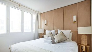 A hotel room with a large bed, two bedside lamps, a nightstand, and a window with curtains. - Apartment in the Center of Paris (Paris)