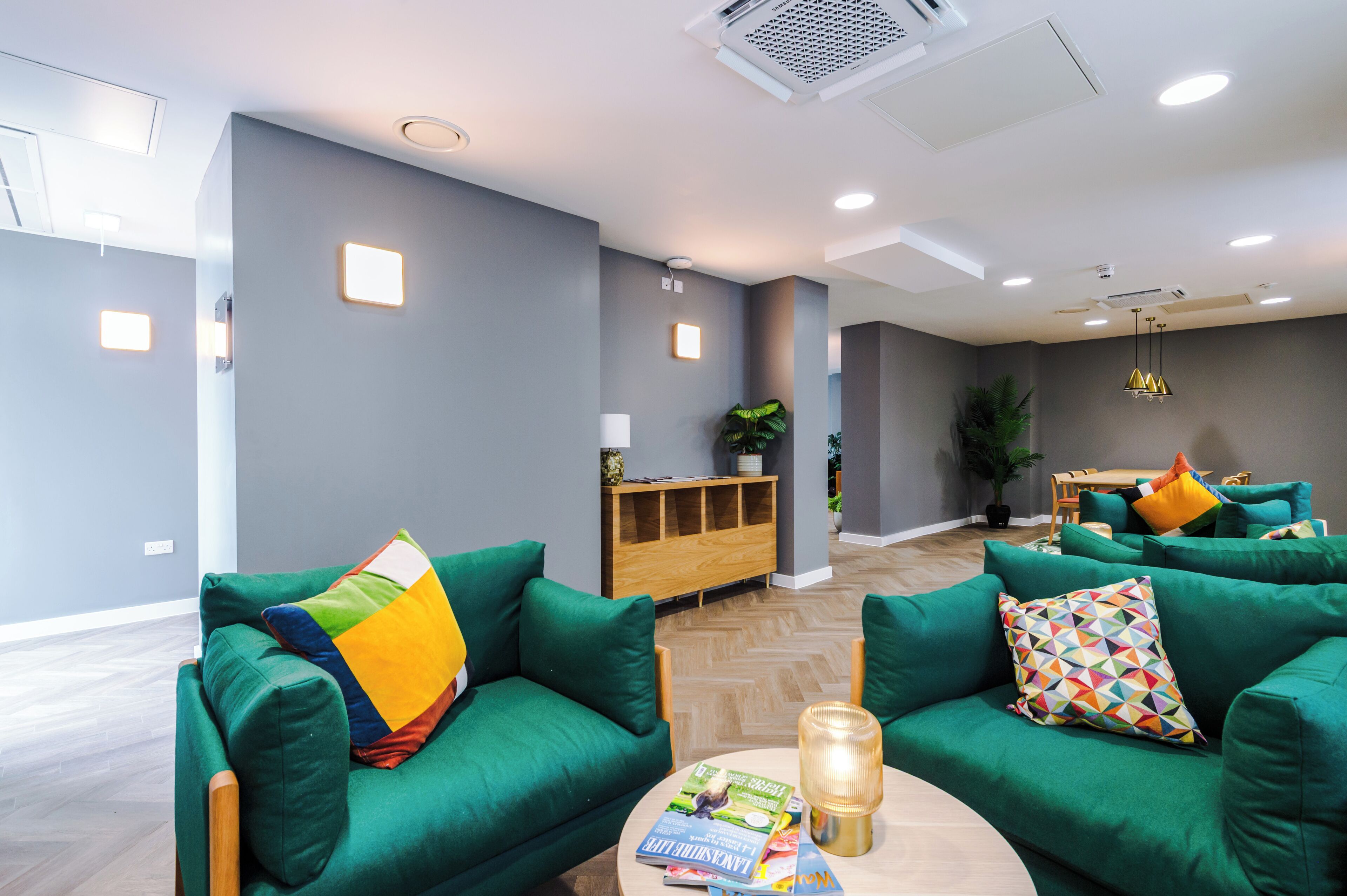 A modern lounge area with green sofas, a wooden sideboard, and a round table with magazines.