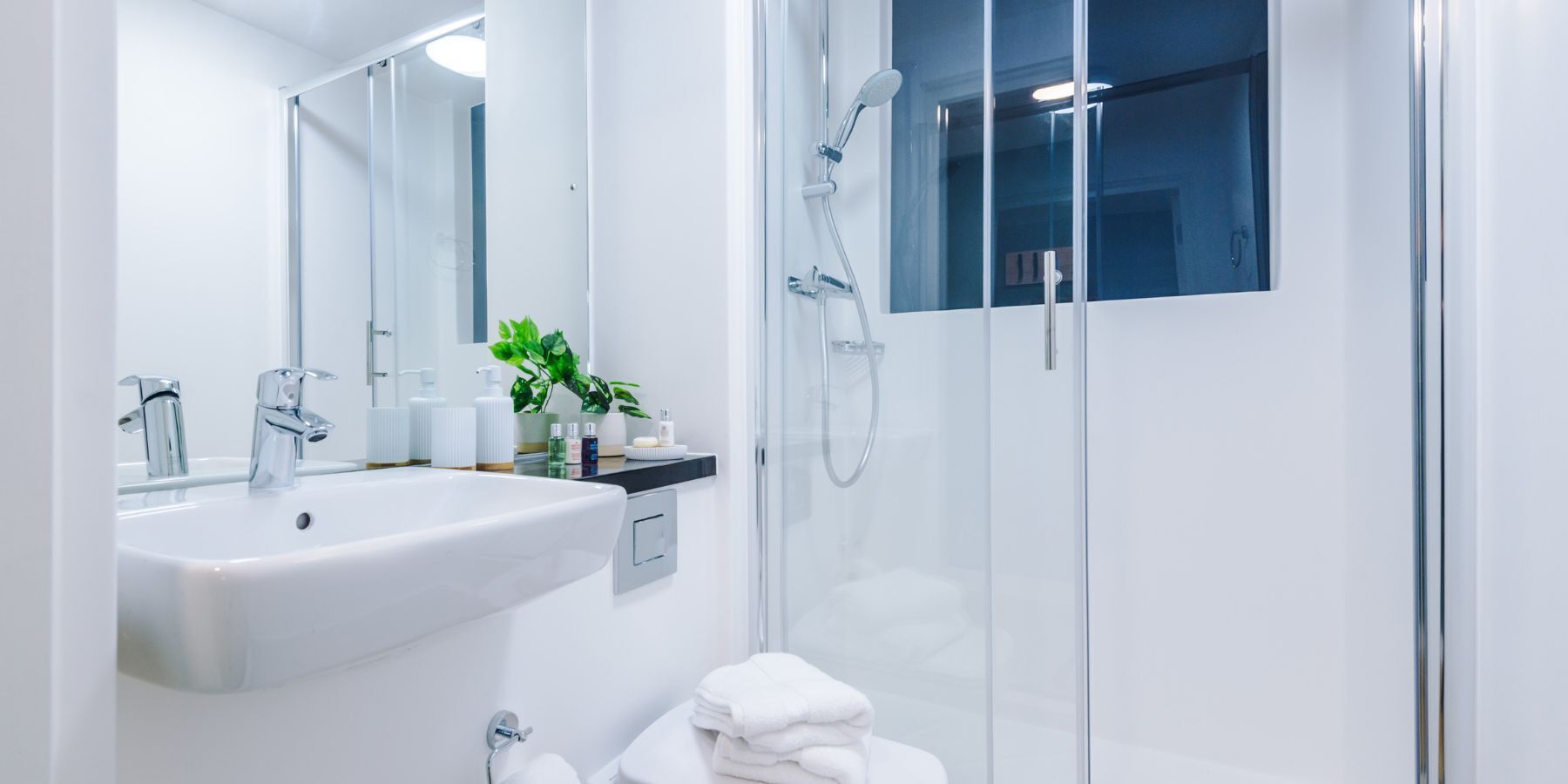 A modern bathroom with a white sink, a glass shower enclosure, and a mirror.