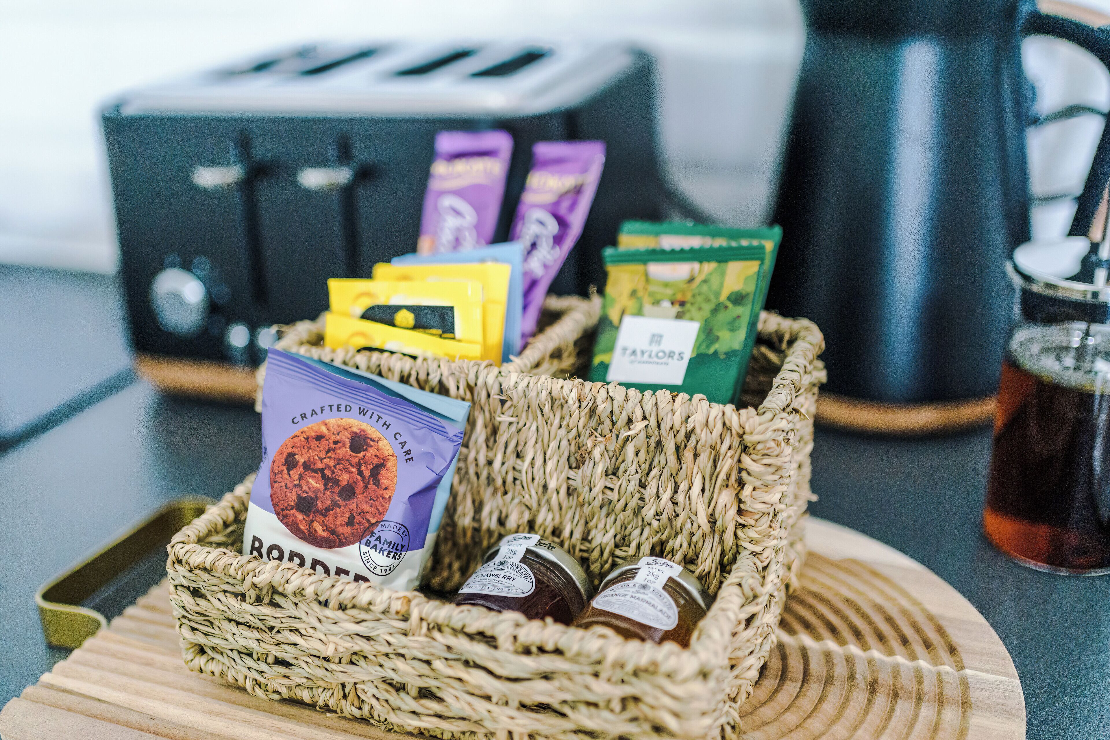 A wicker basket containing packaged food items and a book on a wooden tray.