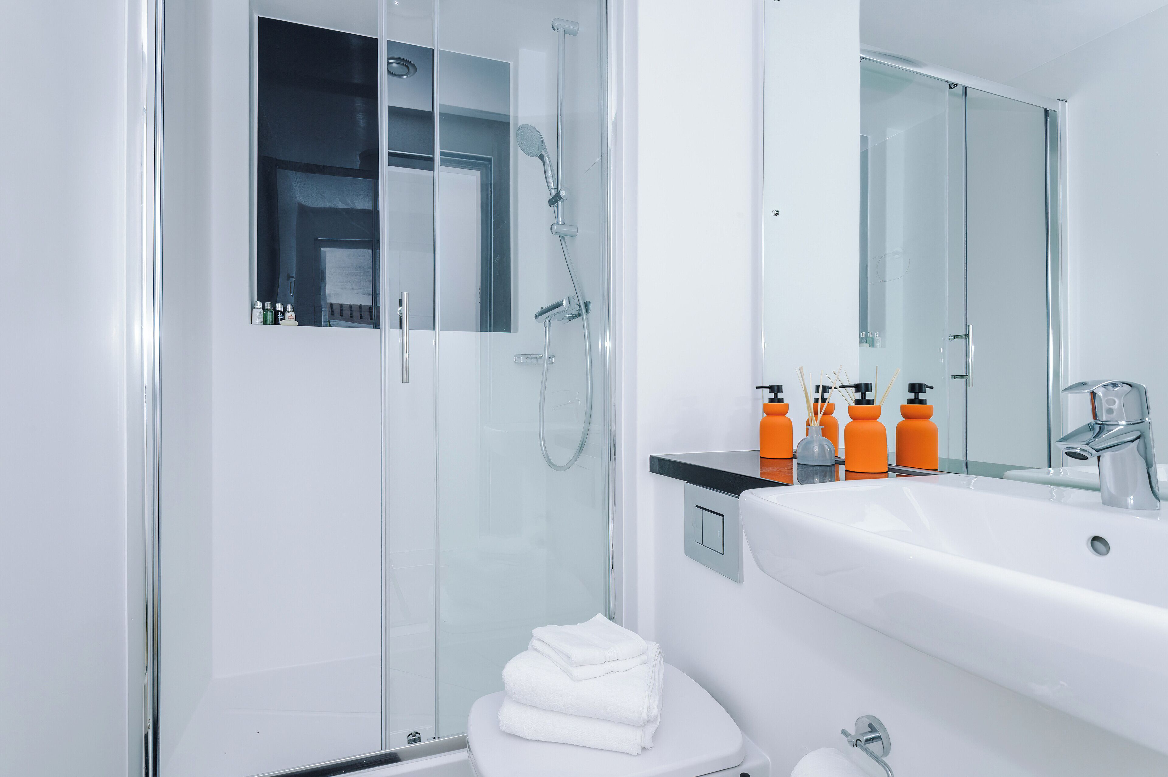 A modern bathroom with a glass-enclosed shower, a white sink, and a large mirror.