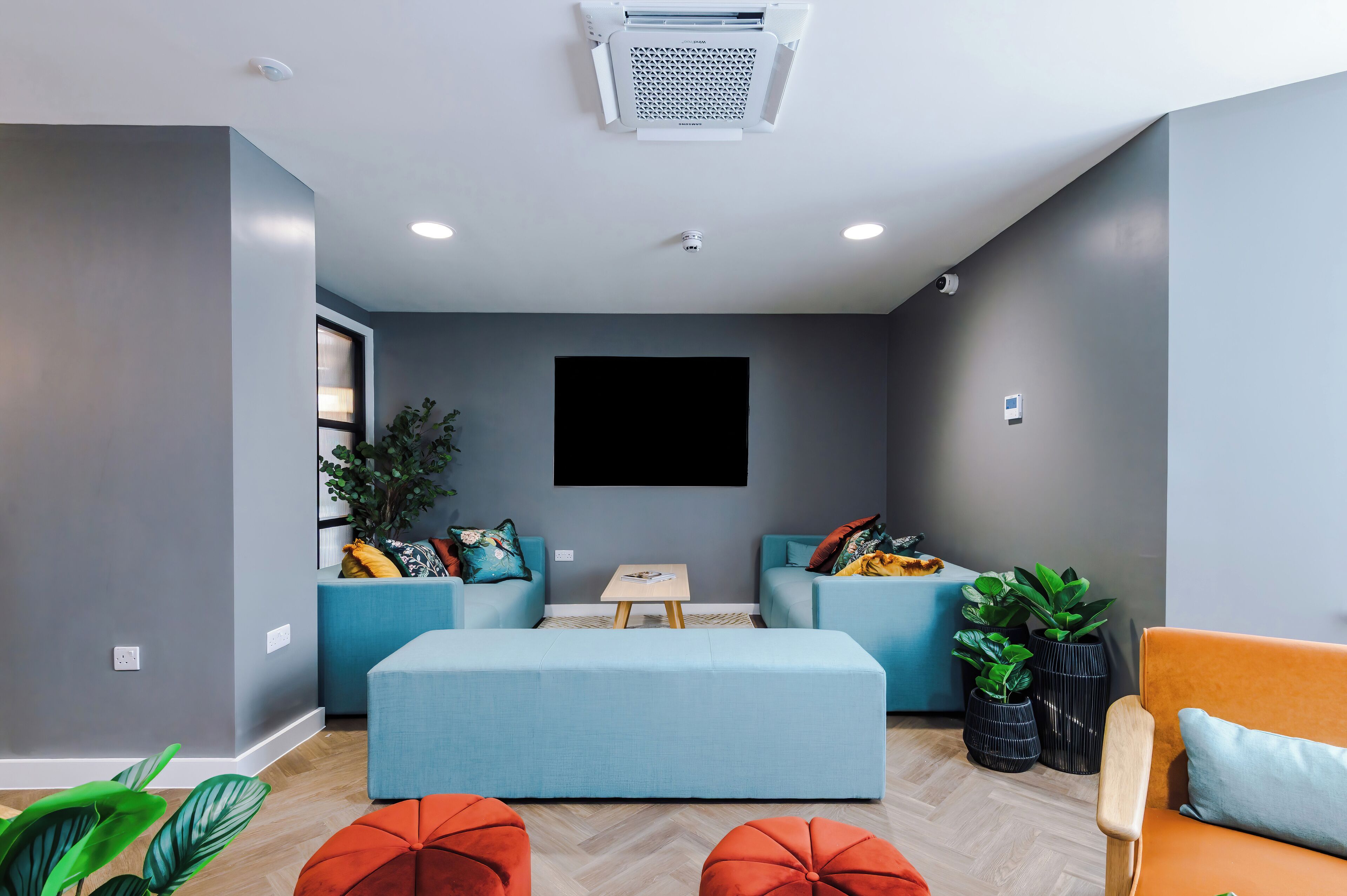 A modern living room with a grey wall, a mounted TV, and a ceiling-mounted air conditioner.