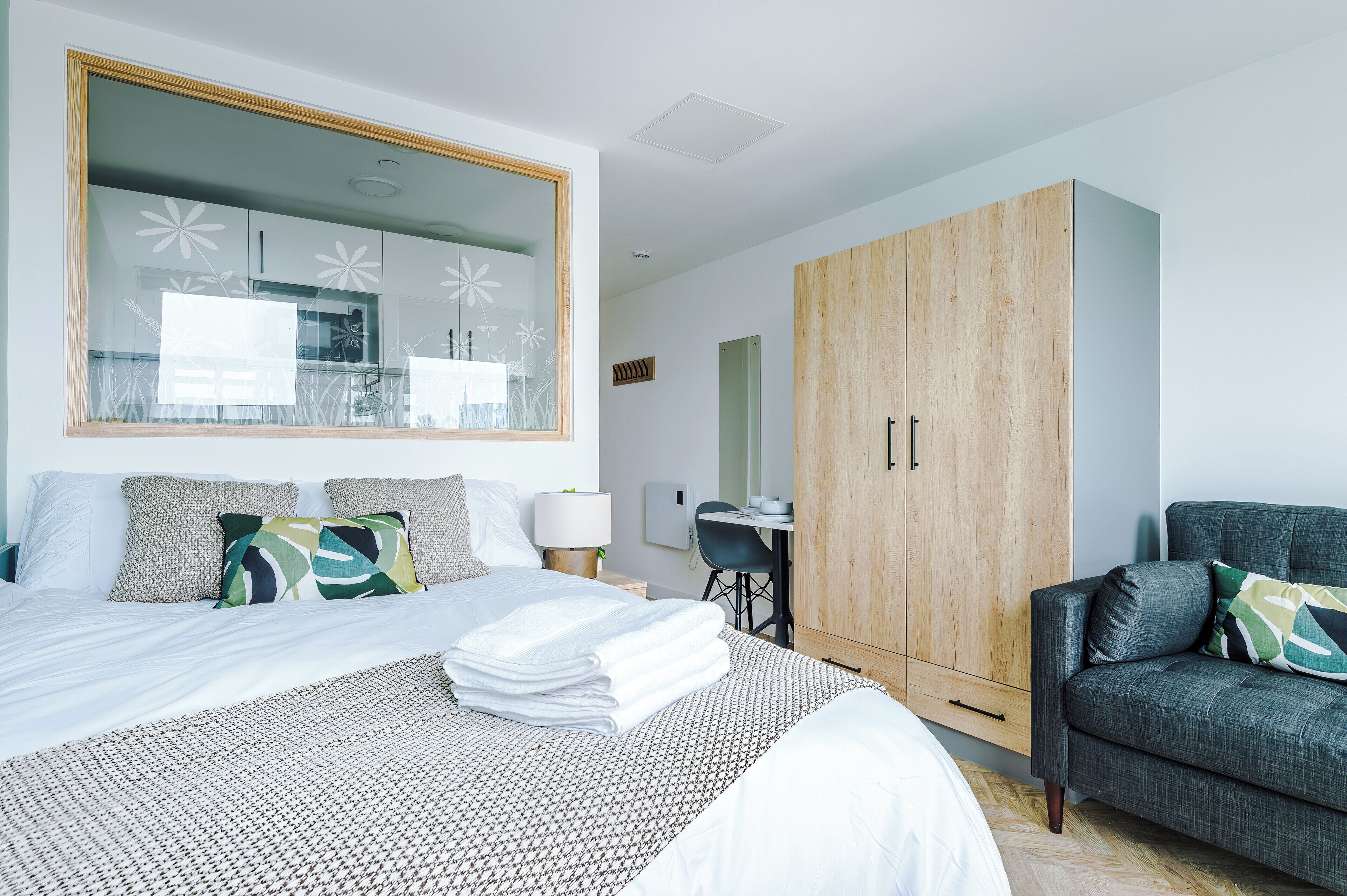 A modern hotel room with a large bed, a wooden wardrobe, a desk, and a comfortable armchair.