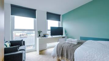 Une chambre moderne avec un lit, un bureau équipé d’un ordinateur et un téléviseur.