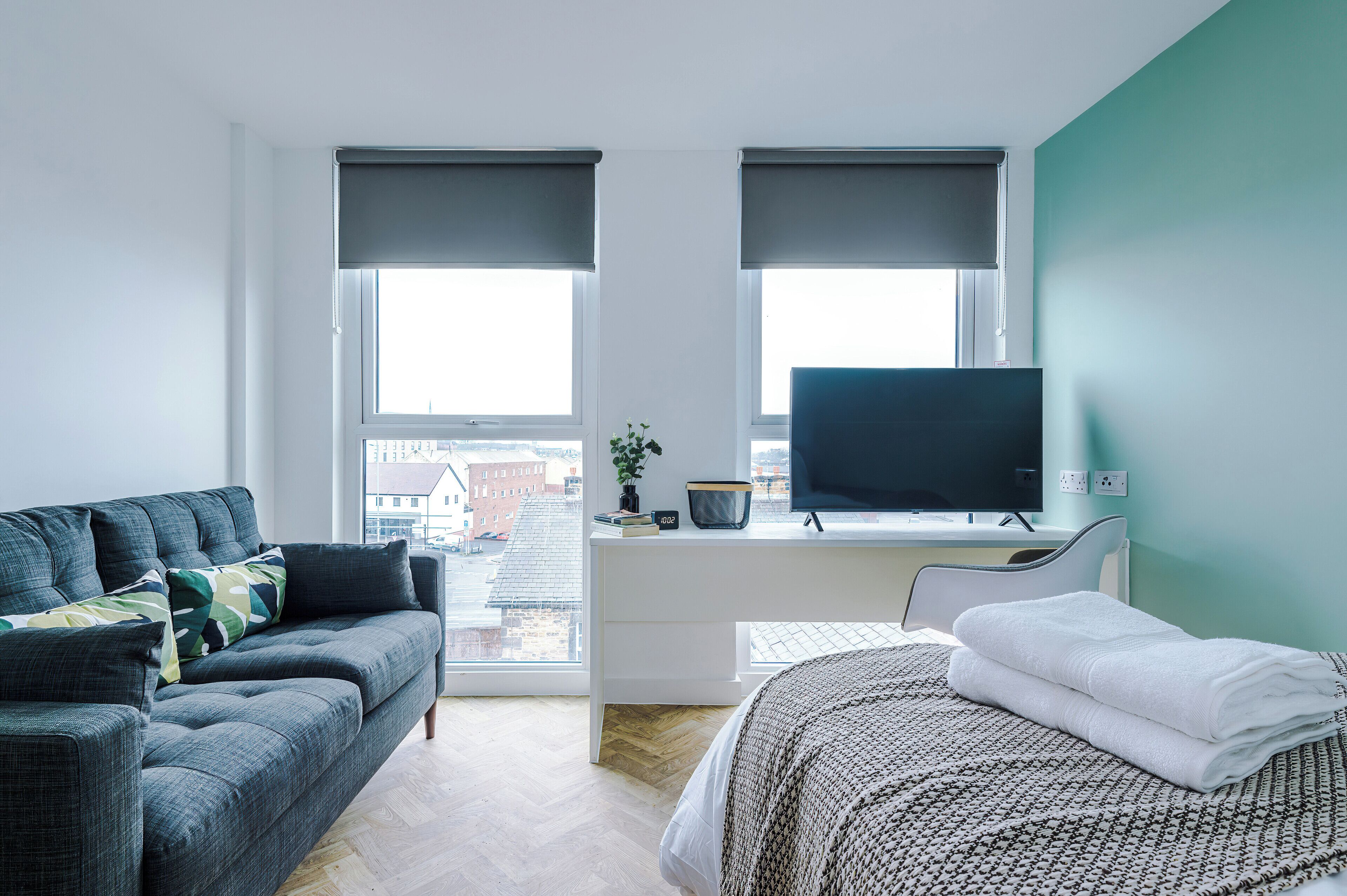 A modern bedroom with a sofa, a bed, a desk with a computer, and a TV.