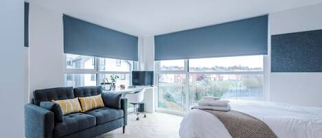 Una habitación de hotel moderna con una cama grande, un sofá, un escritorio con una computadora y vistas a la ciudad.