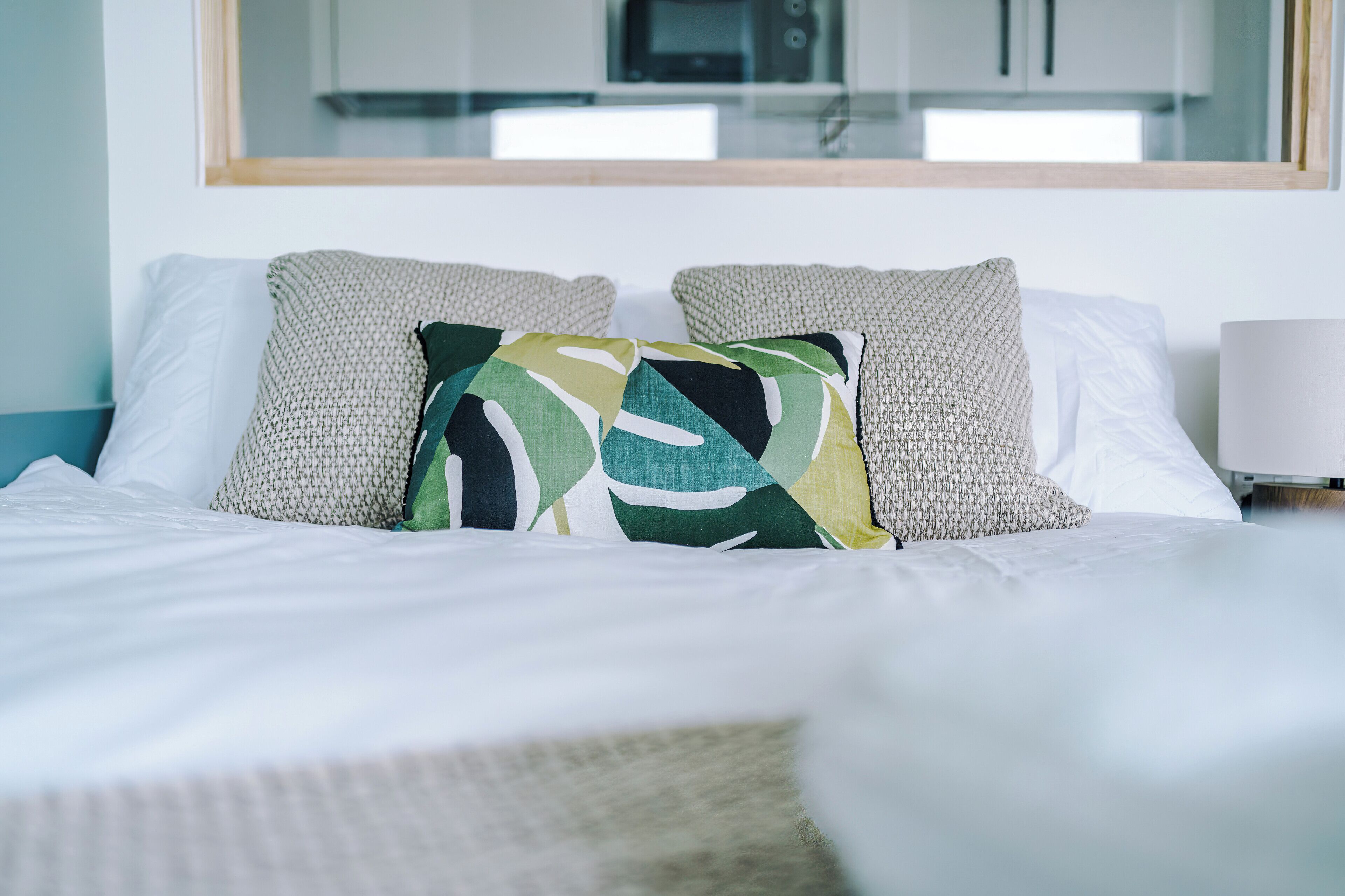 A neatly made bed with white linens and a mix of patterned and solid pillows.