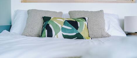 A neatly made bed with white linens and a mix of patterned and solid pillows.