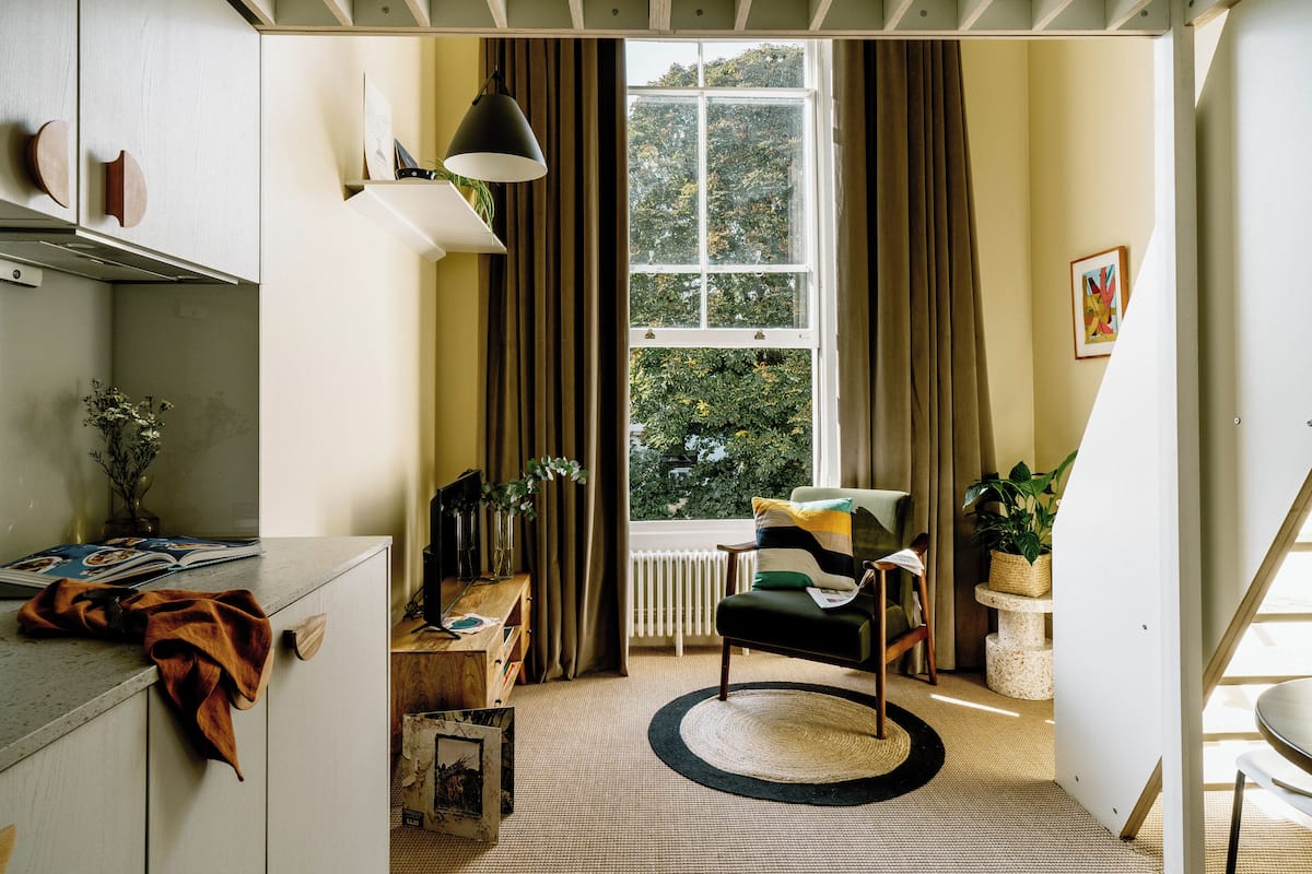 A room with a large window, a chair, a desk, and a bookshelf.