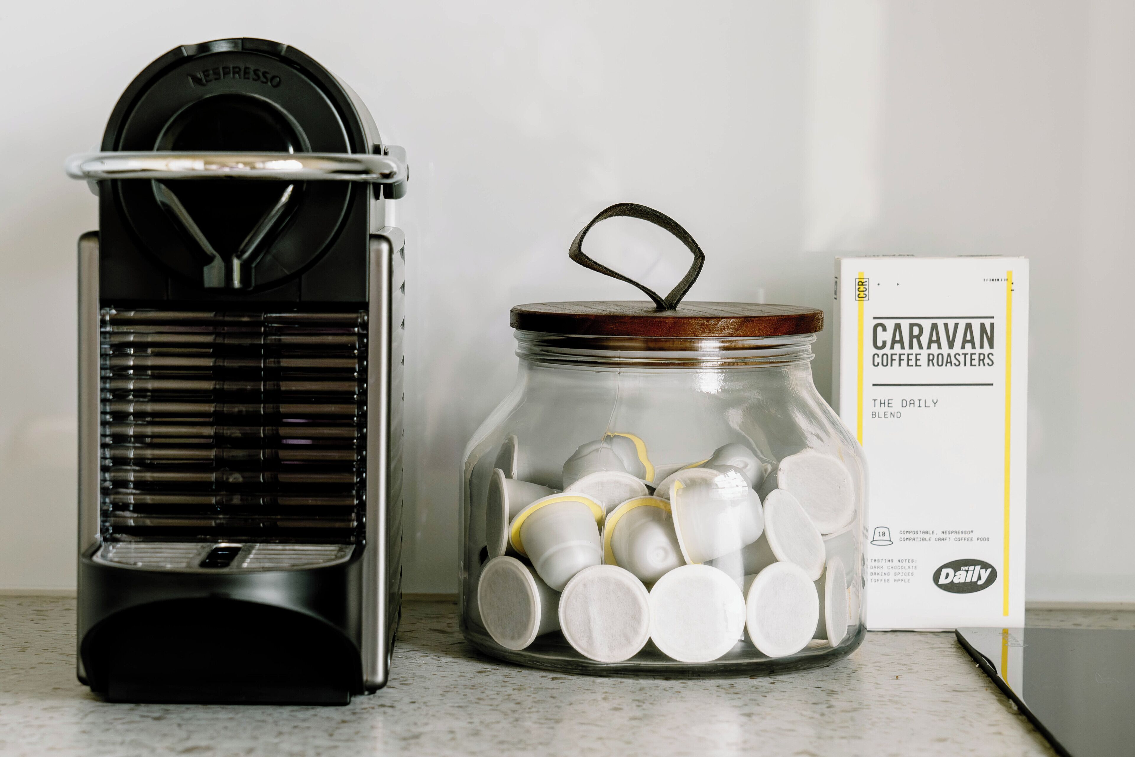 En kaffebryggare och en burk fylld med kaffekapslar, med en förpackning från Caravan Coffee Roasters i bakgrunden.