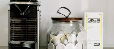 A coffee maker and a jar filled with coffee pods, with a box of Caravan Coffee Roasters in the background.