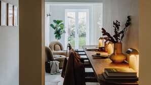 A modern living room with a sofa, a dining table with candles, and a view of a garden through a glass door. - Mason & Fifth, Primrose Hill (London)