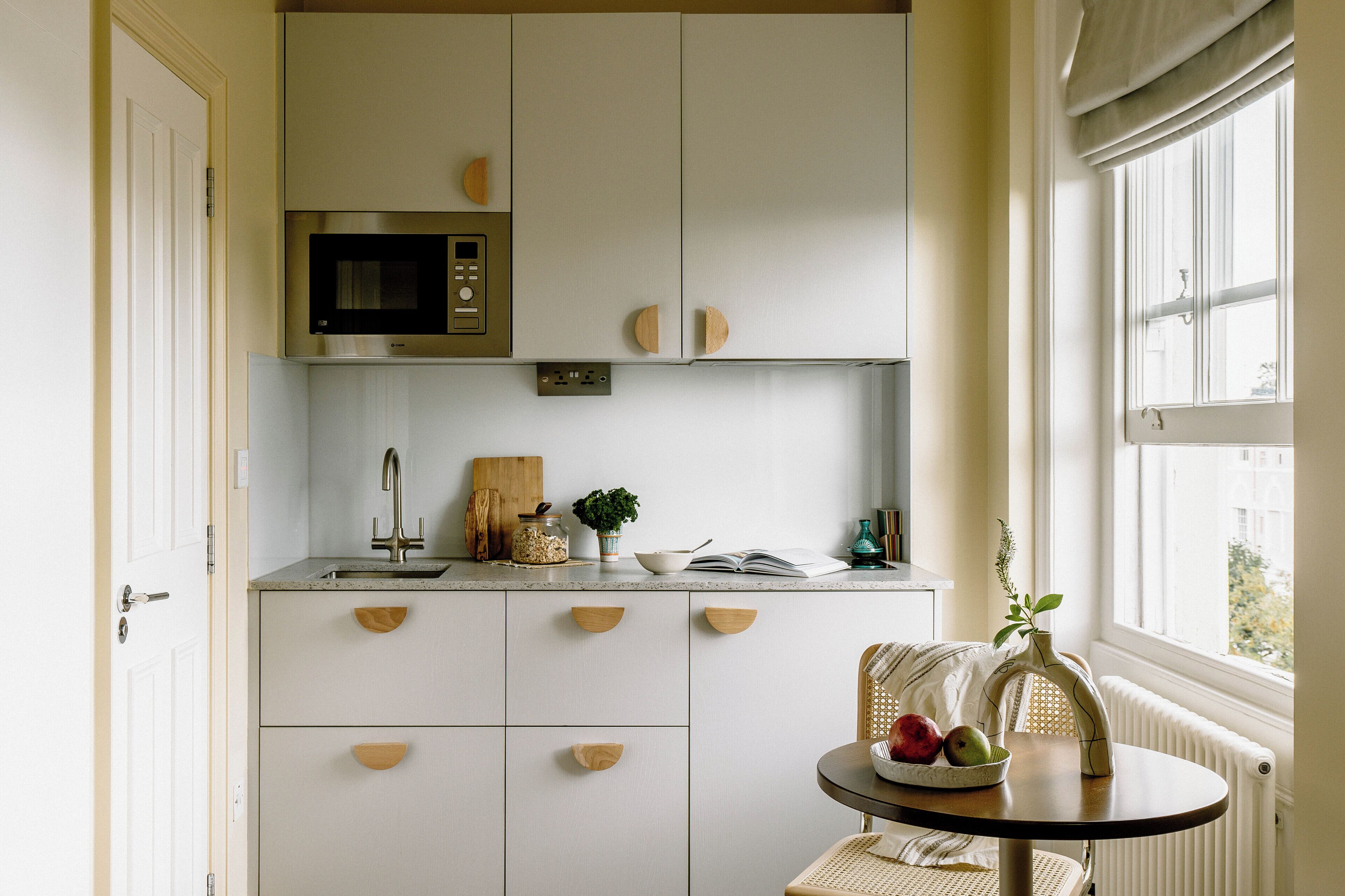 Cocina con armarios blancos, microondas y ventana con vistas.