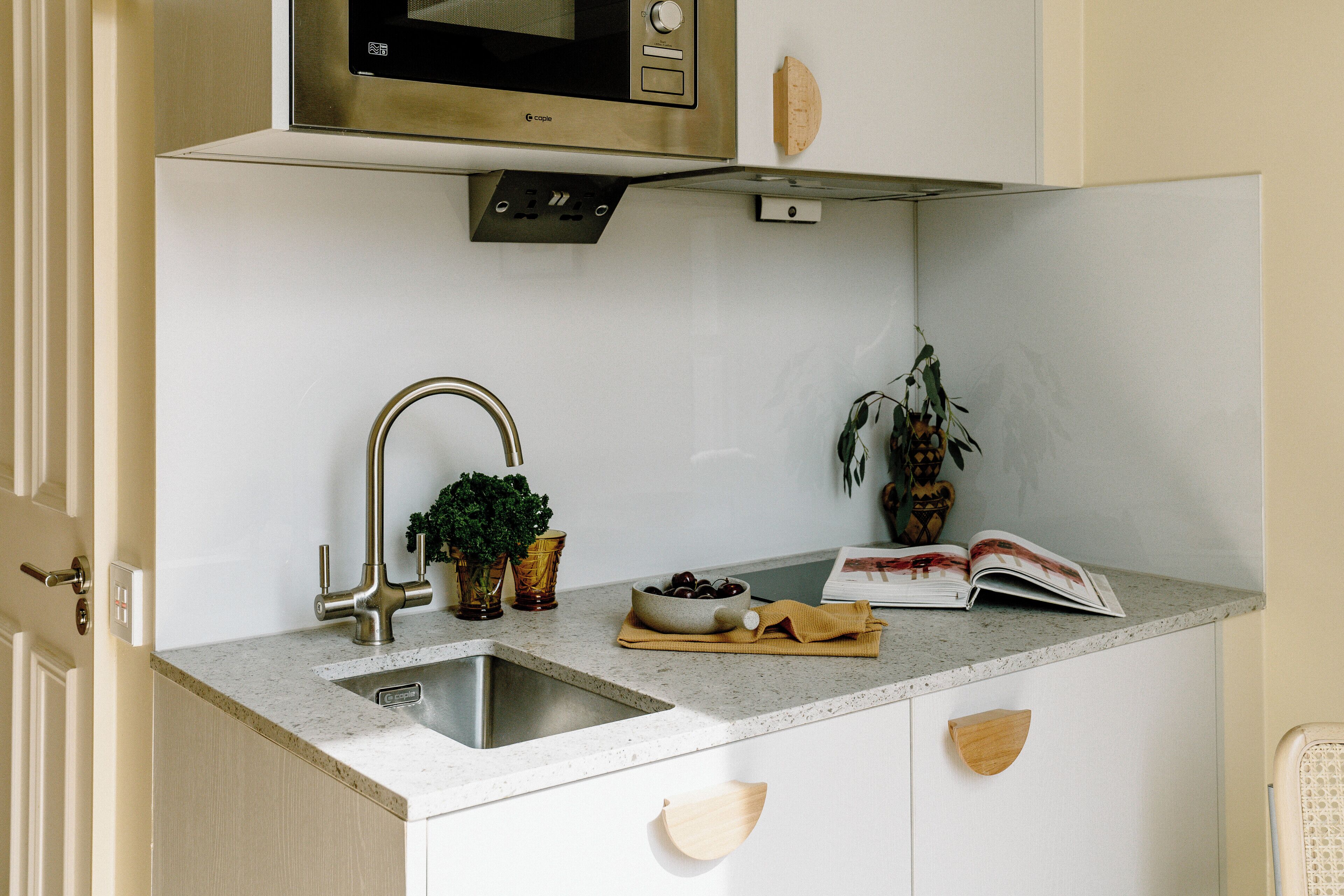 Cocina compacta con microondas integrado, lavamanos de acero inoxidable y armarios de madera.