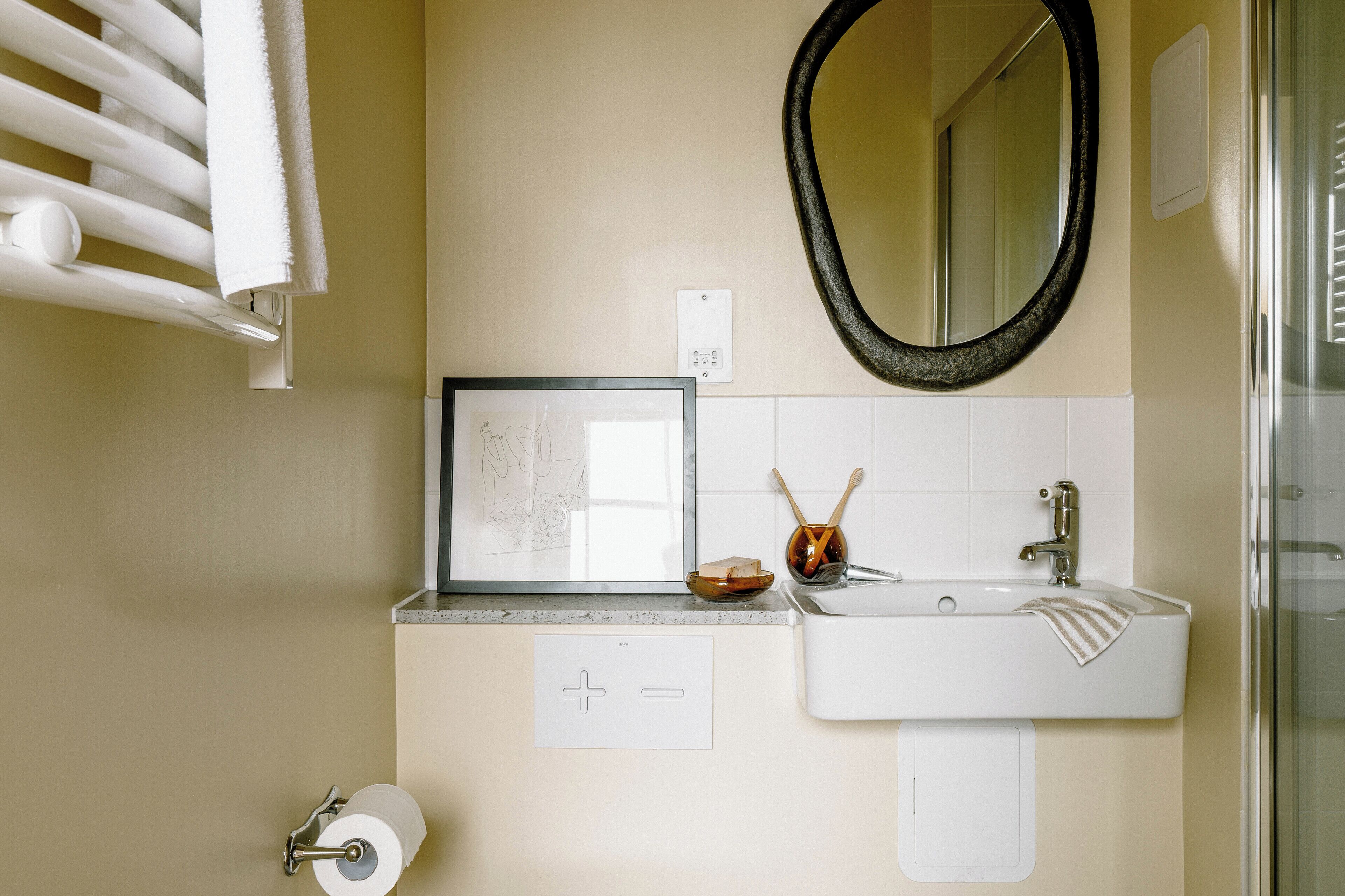 A bathroom with a white sink, a mirror, a framed picture, and a towel rack.