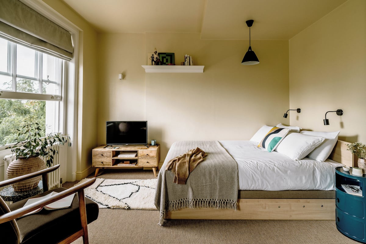 A bedroom with a bed, bedside tables, a TV, and a window with a view of greenery.