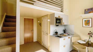 Cocina compacta con microondas, pileta y pequeño comedor con una silla y una mesa.