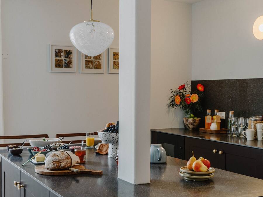 A modern kitchen with a marble countertop, a dining area with a wooden table, and a black backsplash.