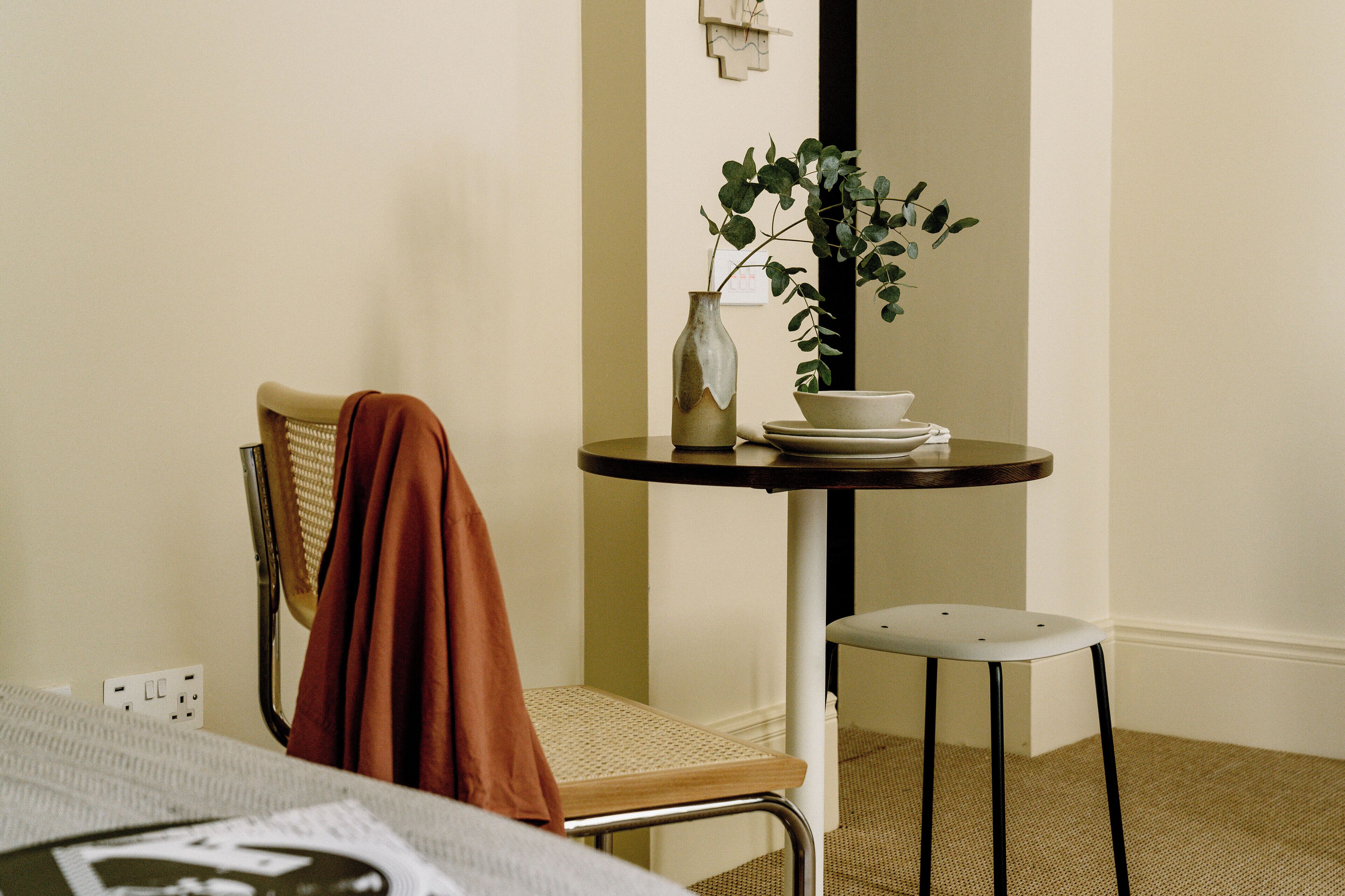 Une pièce comprenant un lit, une chaise, une petite table avec une plante et une étagère fixée au mur.