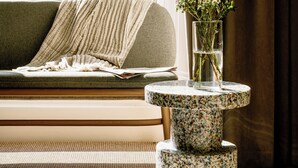 A cozy living room with a sofa, a round table with a vase of flowers, and a view of a stone building through a window. - Mason & Fifth, Primrose Hill (London)