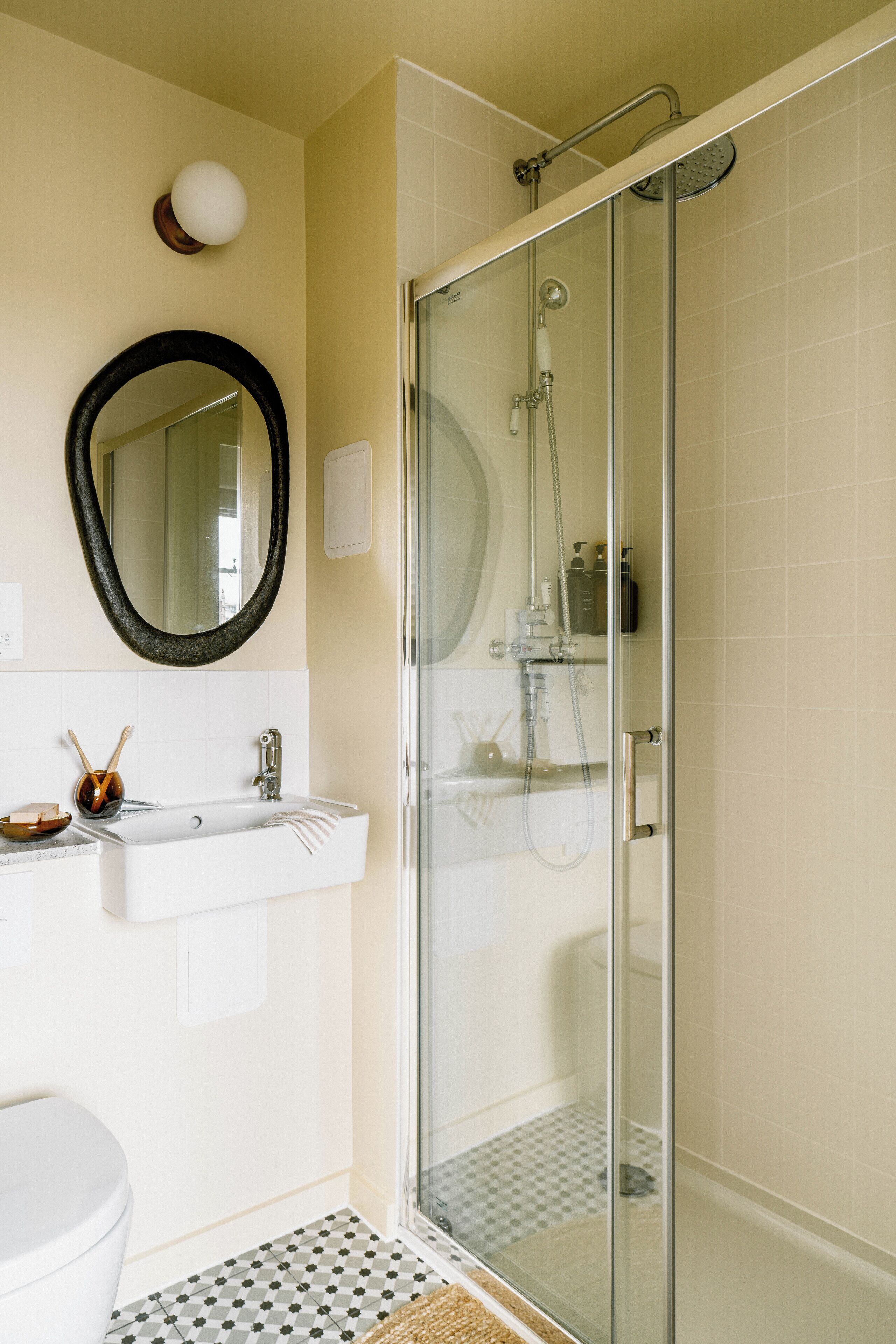 A bathroom with a glass-enclosed shower, a white sink with a mirror above it, and a toilet.