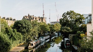 A canal with boats, trees, and buildings in the background. - Mason & Fifth, Primrose Hill (London)