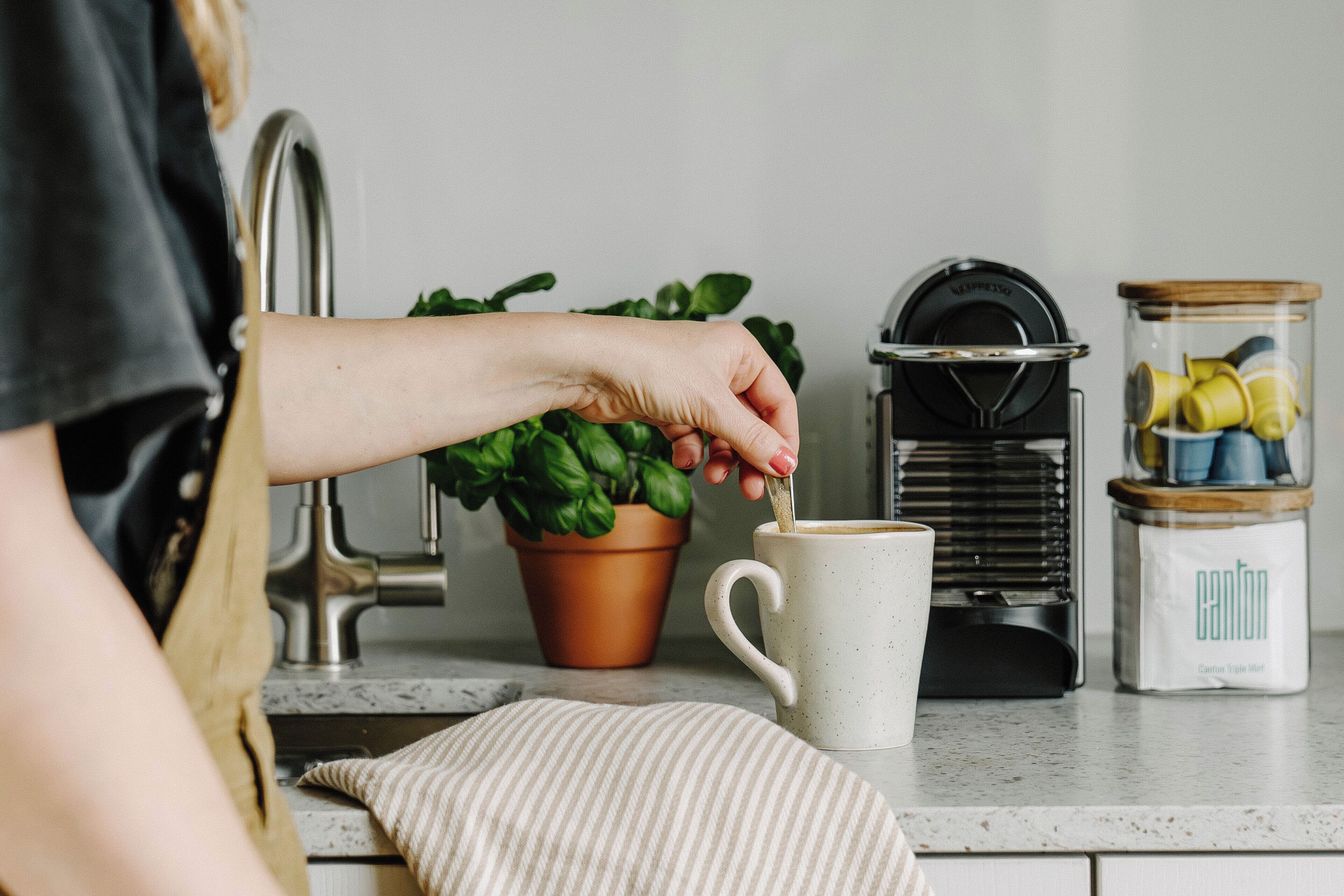 Ένας πάγκος κουζίνας με μια καφετιέρα, ένα φυτό σε γλάστρα και ένα βάζο με ζάχαρη.