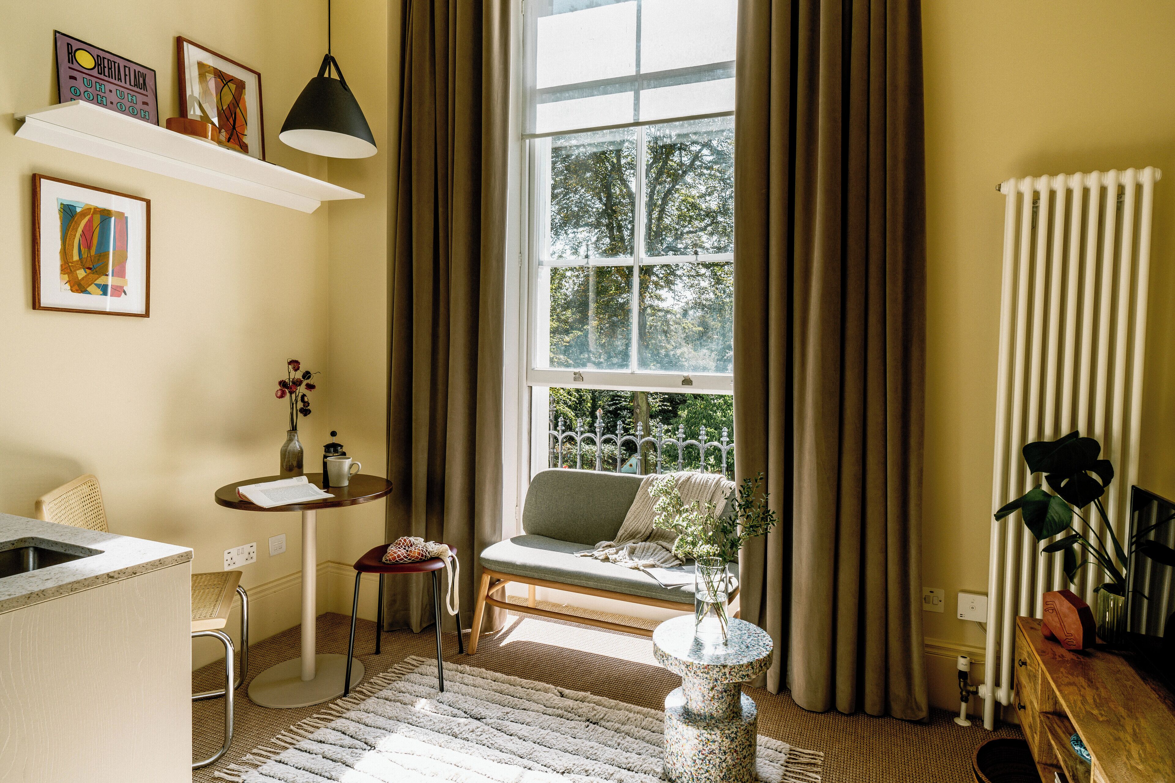A cozy living room with a sofa, a small table, a vase with flowers, and a window with curtains.