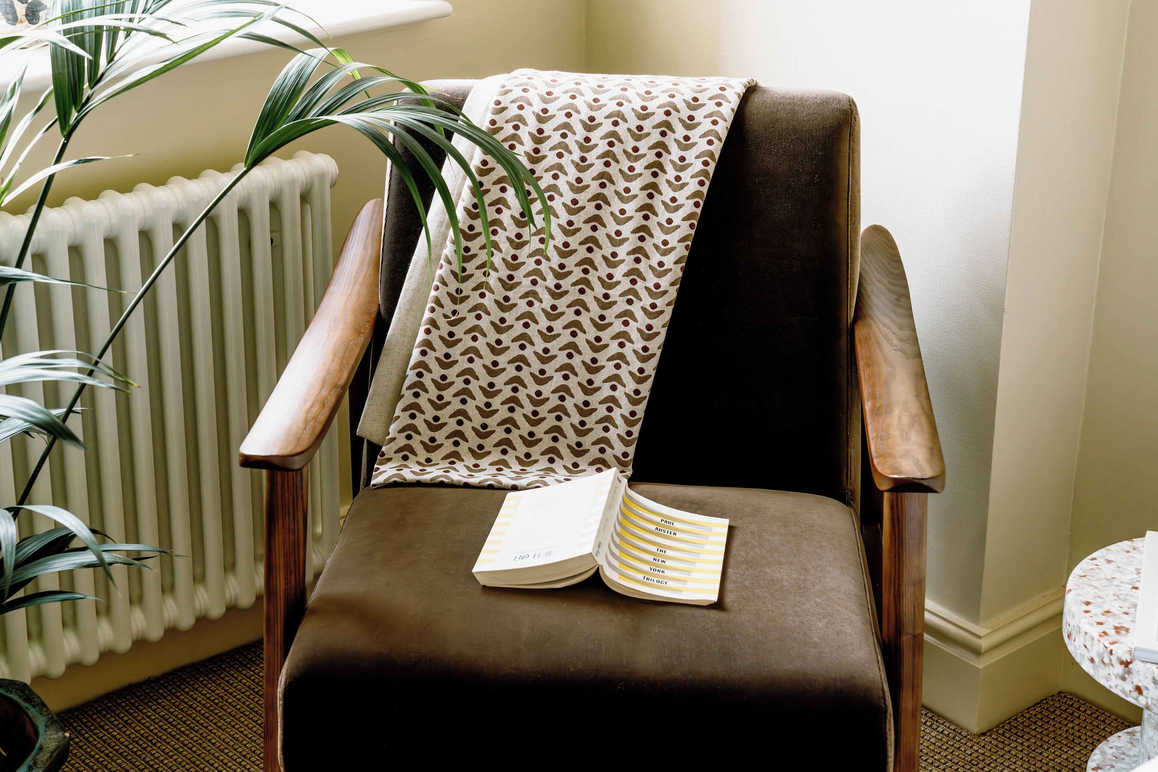 A chair with a book, a patterned throw, and a potted plant.