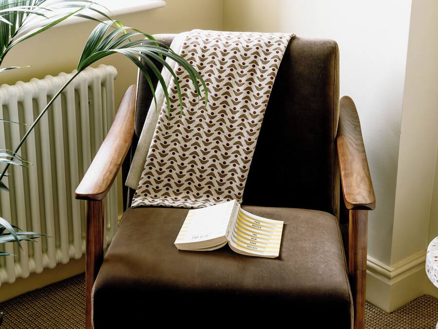 A chair with a book, a patterned throw, and a potted plant.