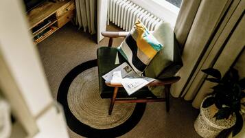 Una habitación acogedora con un sillón verde, una mesita de madera, un tapete tejido y una planta en maceta.