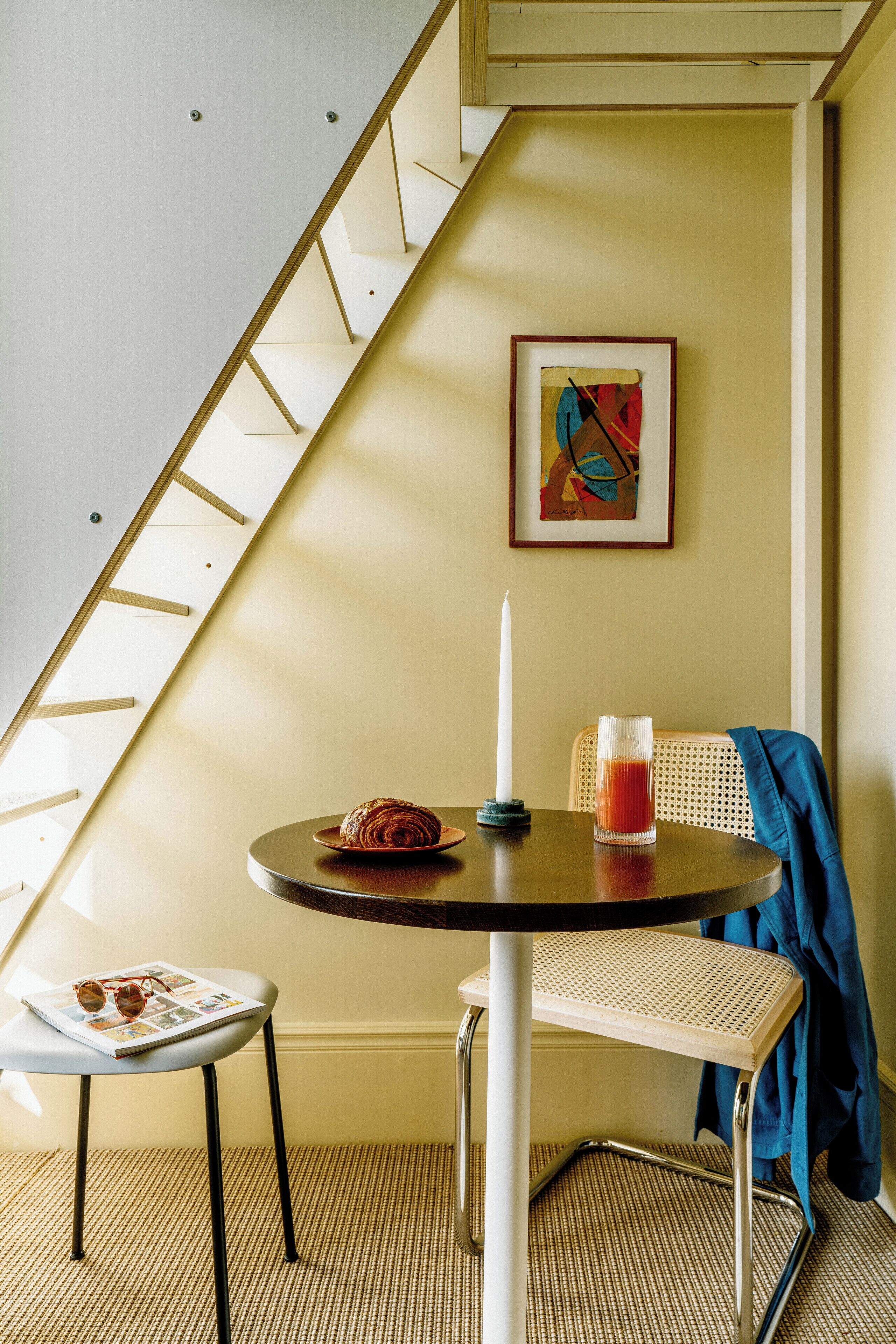 Een gezellig eetgedeelte met een ronde tafel, een stoel, een kaars en een lijst met een kunstwerk aan de muur.