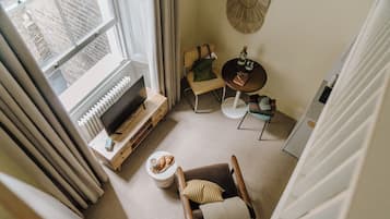 Una habitación acogedora con chimenea, un sillón cómodo, una mesita con una botella y copas, y vistas de la ciudad a través de una ventana.