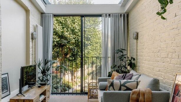 A cozy living room with a grey sofa, a wooden side table, a flat-screen TV, and a large window with curtains. - Mason & Fifth, Primrose Hill (London)