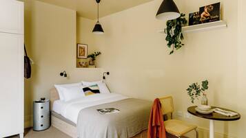 A neatly arranged bedroom with a bed, bedside table, chair, and a small table with a plant.