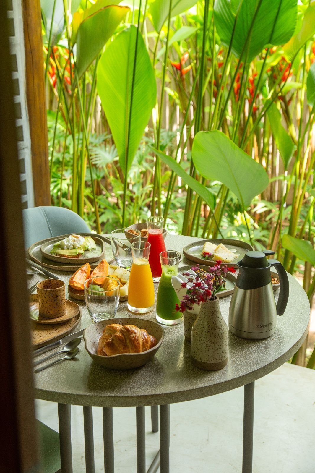 A breakfast table set outdoors with various food items, drinks, and a coffee pot.