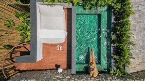 A small outdoor hot tub area with a wooden bench and a green door leading to a pool. - Vila Almesca (Porto Seguro)