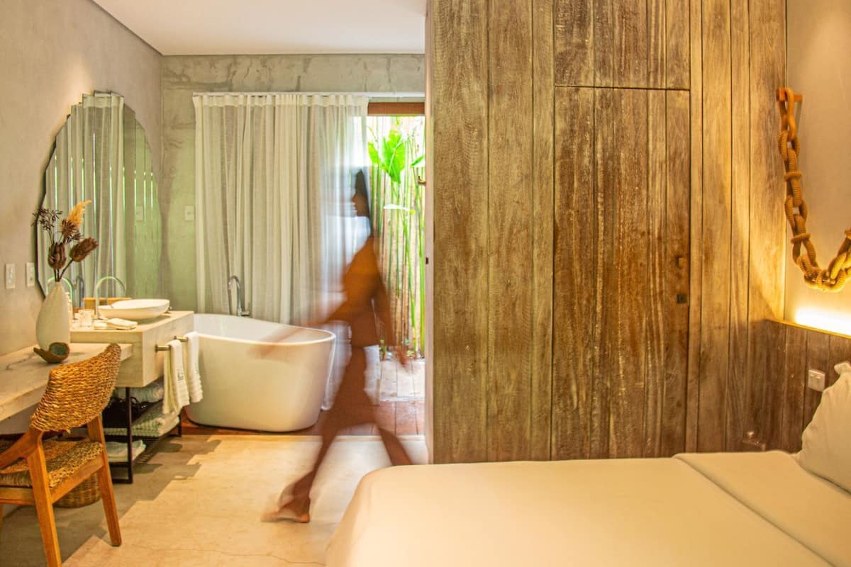 A hotel room with a bed, a sitting area with a chair and a table, a bathtub, and a large mirror.