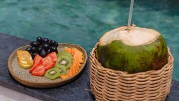 A plate of fruit and a coconut with a straw in a basket by a pool.