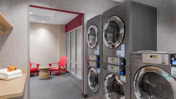 A laundry area with stacked washing machines, a small table with folded towels, and red chairs.