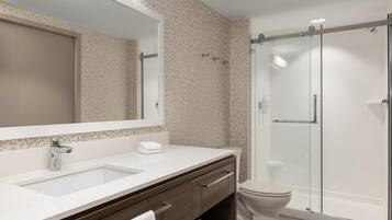 A modern bathroom with a large mirror, a sink, a toilet, and a glass-enclosed shower.