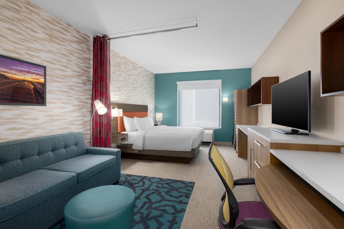 A modern hotel room with a bed, a sofa, a desk, a television, and a window.