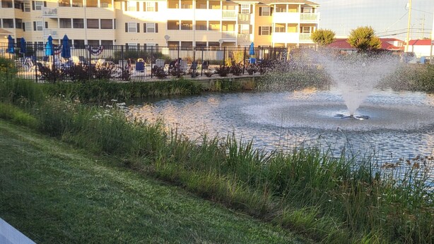 A building with multiple floors, a fenced outdoor area with chairs, and a water feature. - 2103 Palms, 2-bedroom condo, Great Fall Weekends are still available (Rehoboth Beach)