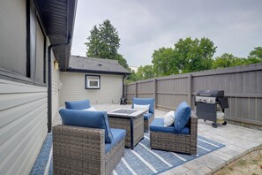 An outdoor patio with wicker furniture, a grill, and a view of a house in the background.