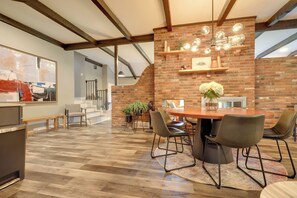 A spacious dining area with a brick wall, wooden ceiling beams, and a large table with chairs. - Chic Family-Friendly Home in Riverside: 7 Mi to KC (Riverside)